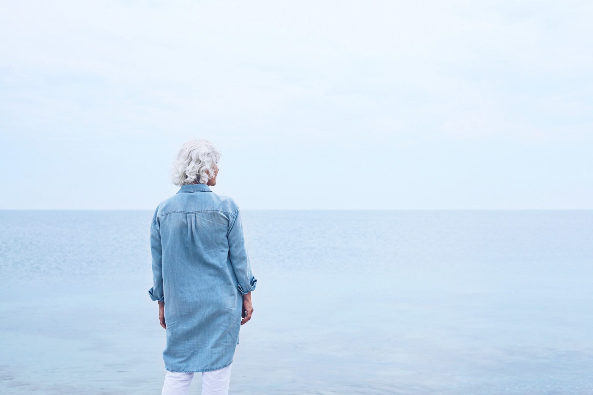 Kvinne står med ryggen til og ser utover havet